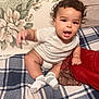 baby, child, curly_hair, onesie, socks, plaid_blanket, pillow, indoor, smiling, cute, infant, person, couch, home, toddler, happy, reaching_hand, soft_furniture, comfortable, portrait