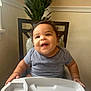 baby, child, high_chair, striped_shirt, smiling, curly_hair, indoor, plant, green_plant, tiled_wall, chair, person, happy, infant, cute, face, table, furniture, light, home
