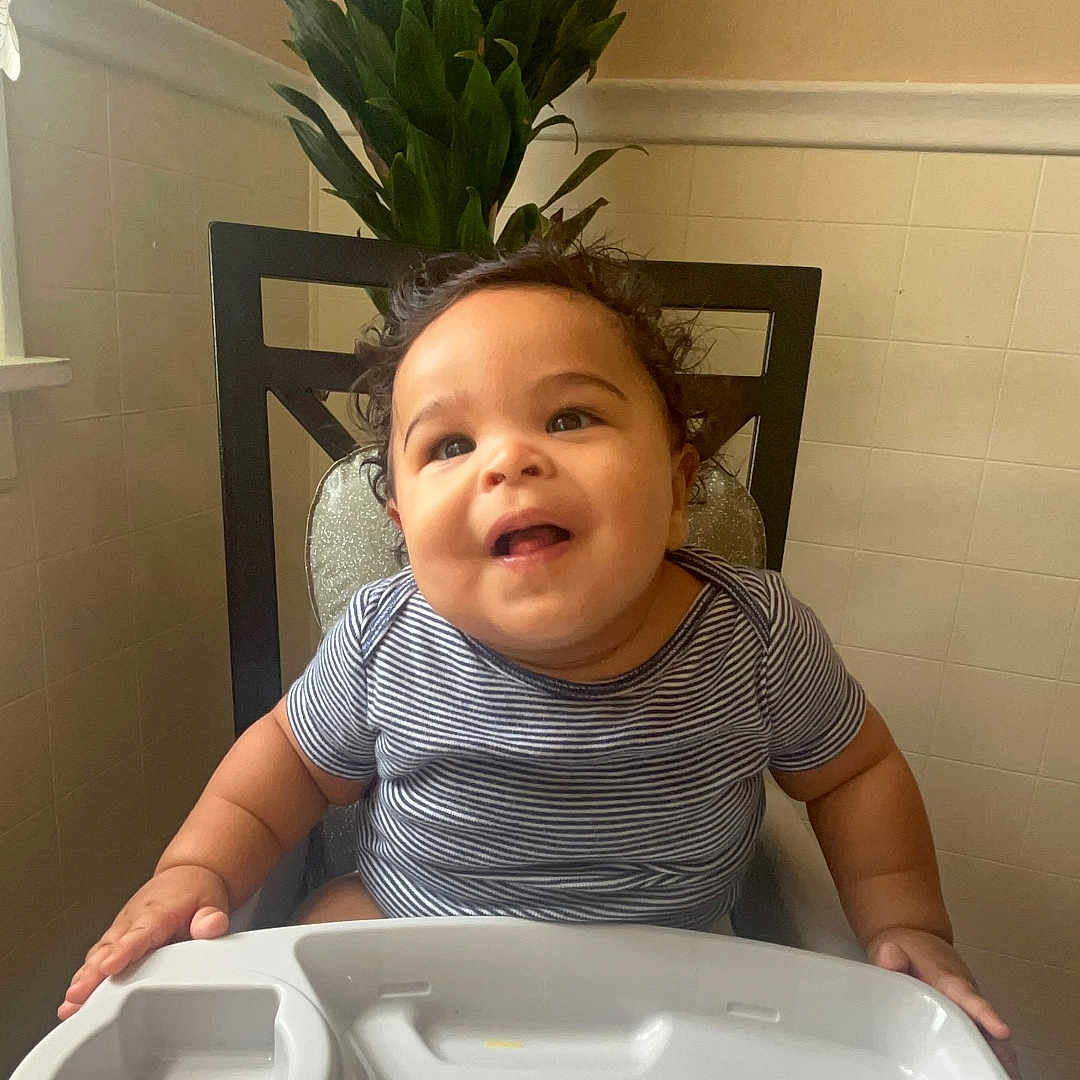 Michael Neil Adames joined the competition — help win amazing prizes! baby, chair, child, curly_hair, cute, face, furniture, green_plant, happy, high_chair, home, indoor, infant, light, person, plant, smiling, striped_shirt, table, tiled_wall