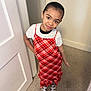 child, girl, red_dress, plaid, white_tshirt, sandals, carpet, door, indoor, smile, pose, standing, person, young, fashion, hair_tied_back, happy, portrait, cute, casual