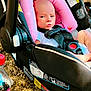 baby, car_seat, pink_cushion, infant, seatbelt, outdoor, ground, rocks, plastic_bottle, beverage, sunlight, shadow, warning_label, black_fabric, child, person, face, head_support, resting, serious_expression