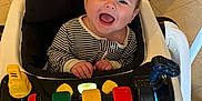 Preston is registered to the contest to win money with this photo: baby, baby_walker, child, colorful, face, floor, hands, happy, head, indoor, person, plastic, play, seat, smiling, striped_onesie, tile_floor, toy, walker_wheels, wood_panel