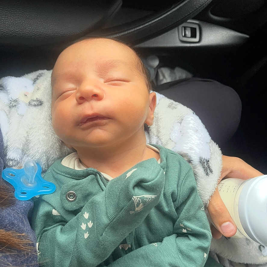 Nasser is registered to the contest to win money with this photo: baby, blanket, bottle, car_interior, child, clothing, cute, feeding, hand, infant, newborn, onesie, pacifier, peaceful, person, resting, seat, sleeping, transportation, young