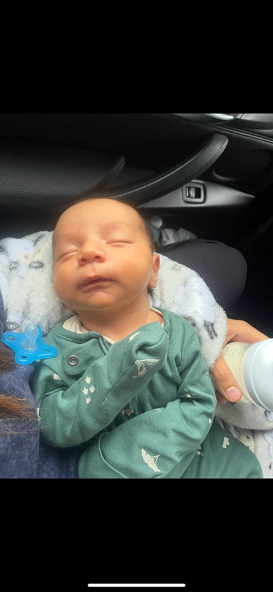 Nasser is registered to the contest to win money with this photo: newborn, baby, sleeping, onesie, pacifier, bottle, hand, car_interior, seat, blanket, infant, child, clothing, person, peaceful, resting, cute, feeding, young, transportation