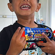 Zenil Patel joined the competition — help win amazing prizes! child, boy, smiling, toy_gun, sonic_the_hedgehog, indoor, black_tshirt, snowman_graphic, happy, portrait, person, short_hair, playful, hand, fingers, teeth, face, casual_clothing, background, home