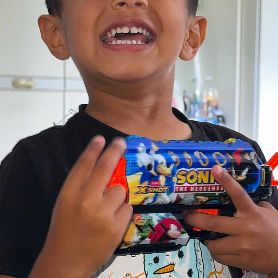 Zenil Patel joined the competition — help win amazing prizes! background, black_tshirt, boy, casual_clothing, child, face, fingers, hand, happy, home, indoor, person, playful, portrait, short_hair, smiling, snowman_graphic, sonic_the_hedgehog, teeth, toy_gun