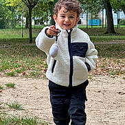 Isaac a rejoint le concours — aidez-le/la à gagner de superbes lots ! child, smiling, outdoor, park, curly_hair, jacket, pants, shoes, grass, trees, path, toy, keychain, happy, person, nature, casual_clothing, walking, daylight, playful