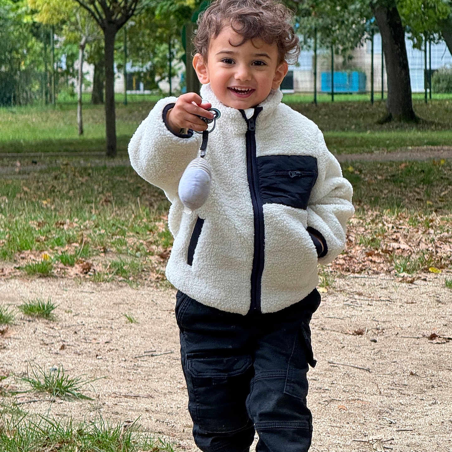 Isaac a rejoint le concours — aidez-le/la à gagner de superbes lots ! casual_clothing, child, curly_hair, daylight, grass, happy, jacket, keychain, nature, outdoor, pants, park, path, person, playful, shoes, smiling, toy, trees, walking