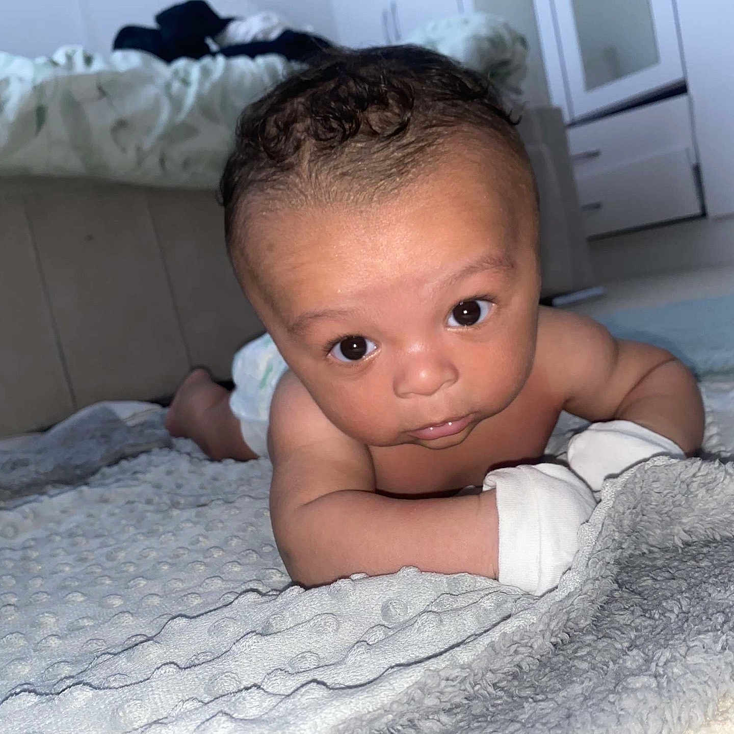 Kairo-Jai is registered to the contest to win money with this photo: baby, blanket, child, closeup, curious, cute, eyes, face, floor, head, home, indoor, infant, mittens, person, skin, soft_lighting, toddler, tummy_time, young