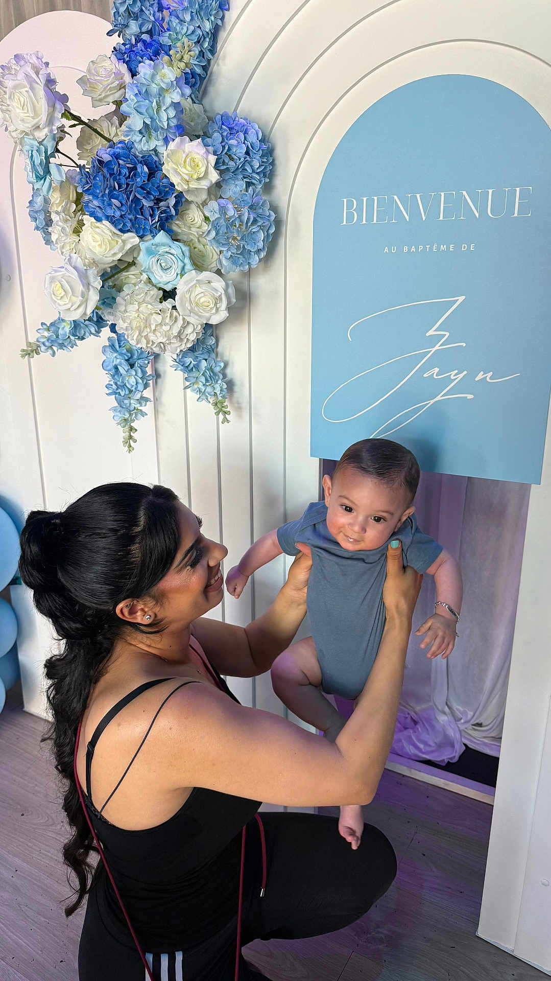 Zayn participe au concours pour gagner de l'argent avec cette photo : baby, baptism, blue, celebration, clothing, decoration, event, floor, flowers, happy, holding, indoors, parent, people, person, portrait, sign, smiling, white, woman