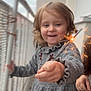 child, toddler, sparkler, smile, balcony, grey_dress, celebration, spark, curly_hair, portrait, happy, hand, railing, bokeh, outdoor, cozy_clothing, holiday, face, person, blurred_background