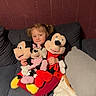 blanket, child, comfort, couch, cushion, cute, girl, home, indoor, mickey_mouse, minnie_mouse, person, pigtails, plush_toys, red_clothing, seated, smiling, soft_toys, tights, toy