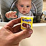 Livio participe au concours pour gagner de l'argent avec cette photo : baby, high_chair, hand, food_container, nesquik, toy, giraffe_toy, indoor, child, curious, reaching, face, person, table, clothing, bib, expression, skin, head, mouth