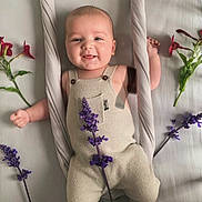 Livio participe au concours pour gagner de l'argent avec cette photo : baby, infant, smiling, romper, flowers, purple_flowers, red_flowers, fabric, rope, soft_surface, cute, child, portrait, happy, skin, hands, feet, laying, indoors, natural_light