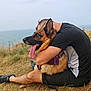Oméga a rejoint le concours — aidez-le/la à gagner de superbes lots ! dog, german_shepherd, person, hugging, outdoor, grass, ocean, casual_clothing, black_shirt, shorts, leash, happy_dog, tongue_out, nature, relaxation, pet, animal, summer, friendship, companionship
