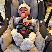 Ezekiel is registered to the contest to win money with this photo: baby, infant, child, car_seat,  안전_harness, hat, knitted_hat, pom_pom, fuzzy_socks, thumb_sucking, sitting, indoors, portrait, front_facing, gray_clothing, seat_belt, safety, nursery, home, cozy