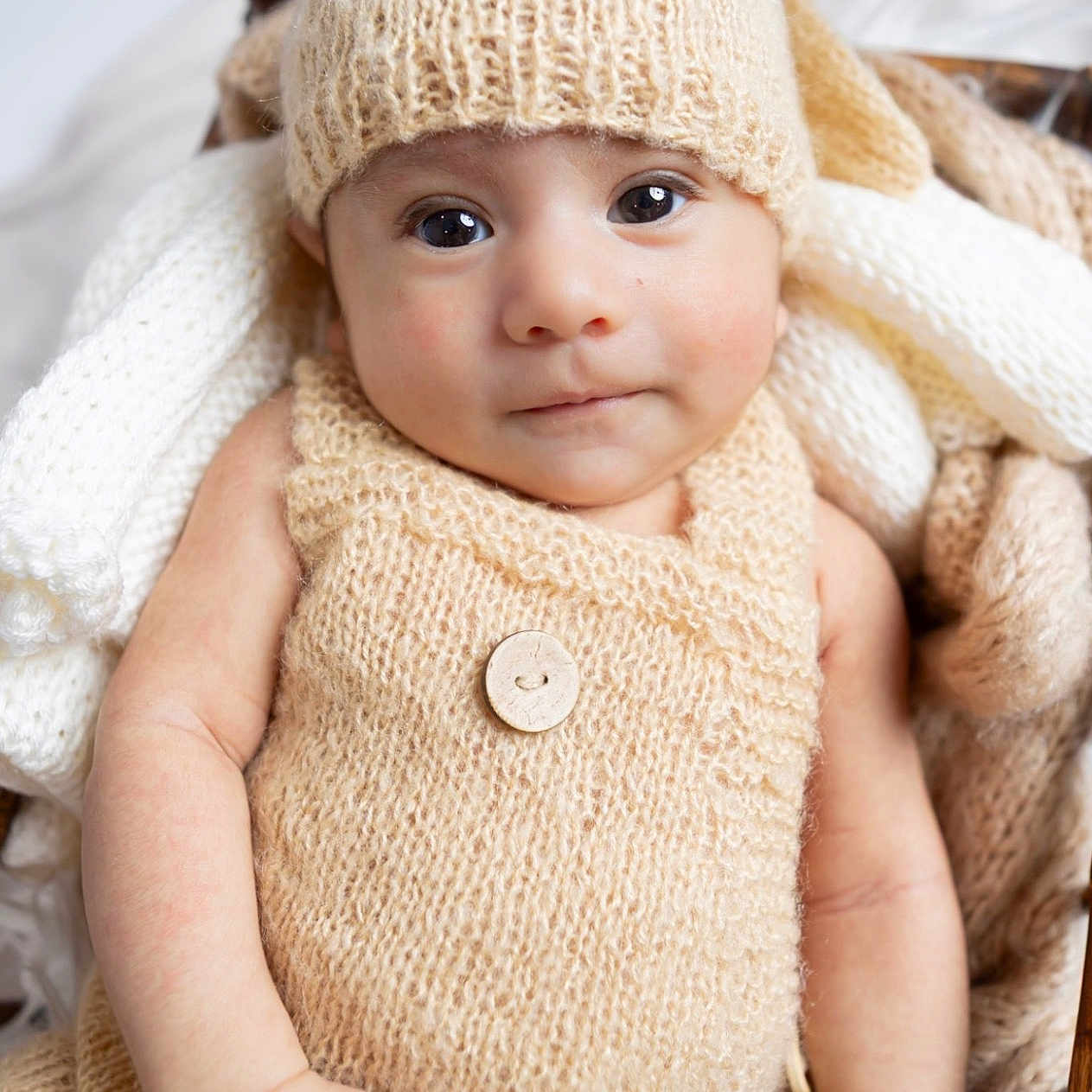 Ezekiel is registered to the contest to win money with this photo: baby, infant, child, portrait, face, eyes, looking_at_camera, neutral_expression, knit_hat, knit_clothing, wool, cream_color, blanket, cozy, indoors, seated, chair, soft_lighting, close_up, photography