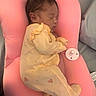 newborn, baby, sleeping, onesie, yellow_clothing, pink_cushion, pacifier, infant, soft_fabric, bedroom, peaceful, cute, resting, indoors, child, face, head, small_person, baby_sleeping, cozy