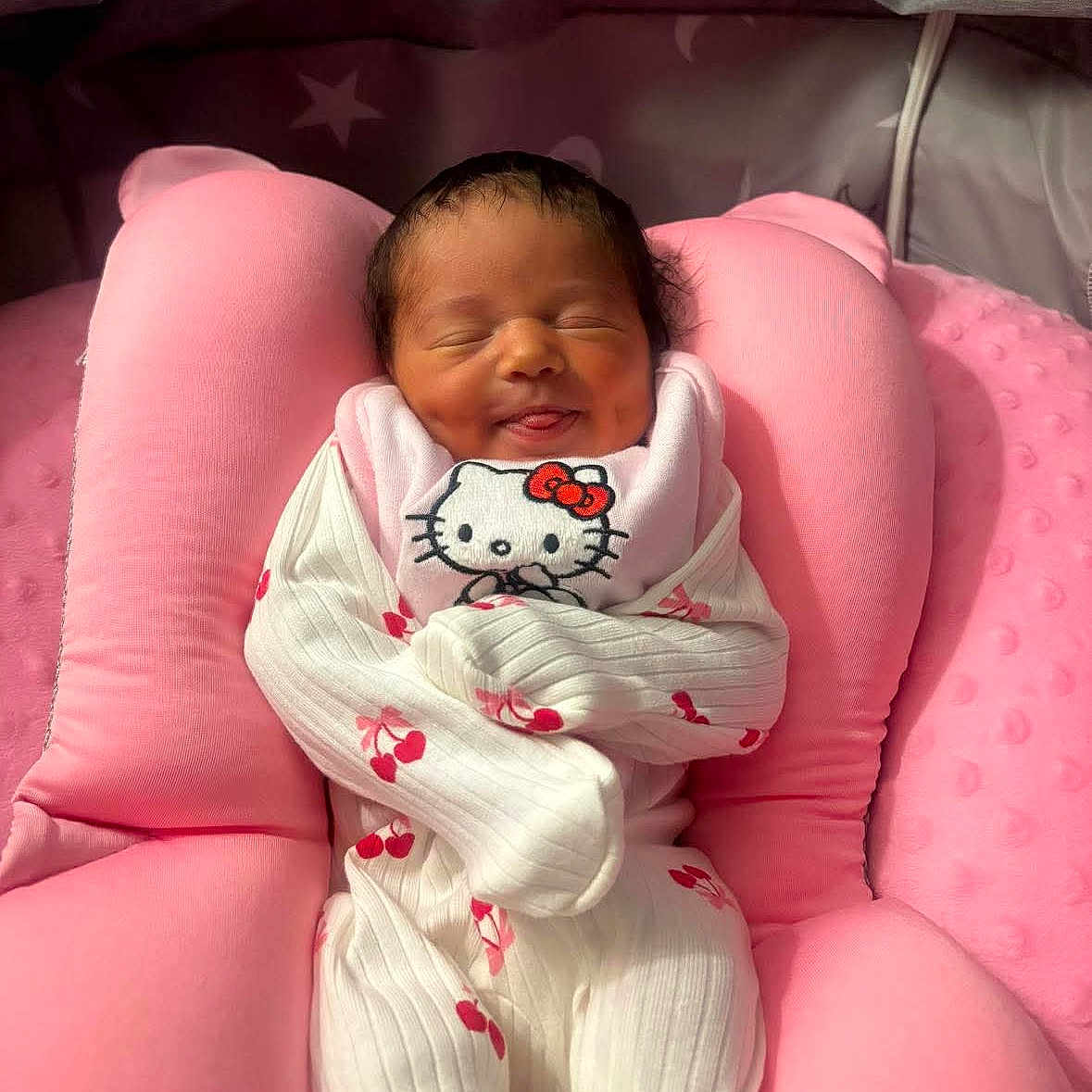 Sienna joined the competition — help win amazing prizes! newborn, baby, infant, pink_cushion, hello_kitty, onesie, cherry_pattern, smile, dimples, tongue_out, cozy, soft_light, sleepy, cute, indoors, portrait, wrapped, child, resting, comfortable