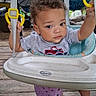 baby, baby_seat, child, curly_hair, face, feet, gray_shirt, handles, infant, jumper, outdoor, photography, play_equipment, portrait, serious_expression, sitting, straps, toddler, toy, wooden_deck