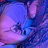 Waffles is registered to the contest to win money with this photo: man, cat, sleeping, arm, bed, pillow, blanket, indoor, rest, cozy, relaxation, pet, human, animal, nighttime, purple_light, blue_light, facial_hair, tshirt, cuddle
