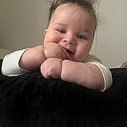 Malakai is registered to the contest to win money with this photo: baby, child, face, hand, cushion, curly_hair, indoor, resting, cute, smiling, skin, white_clothing, closeup, portrait, infant, soft_texture, blue_eyes, cheeks, baby_pose, fingers
