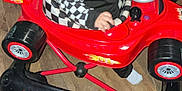 Malakai joined the competition — help win amazing prizes! baby, child, toy_car, indoor, floor, red_couch, curly_hair, blue_eyes, clothing, black_and_white, checkered_pattern, plastic, wheels, seat, person, infant, wood_floor, furniture, playtime, expression