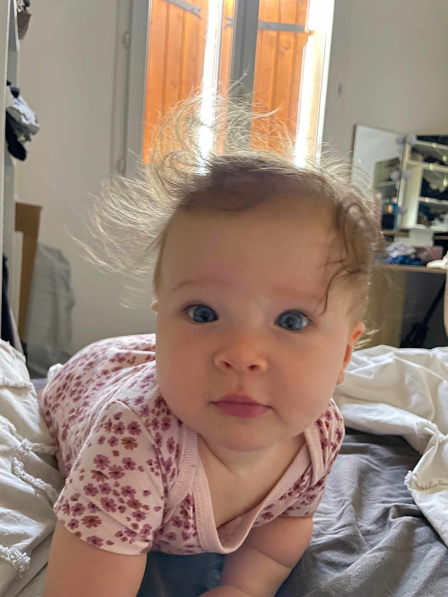 Jane participe au concours pour gagner de l'argent avec cette photo : baby, infant, face, blue_eyes, hair, curly_hair, bed, blanket, clothing, pink_flower_pattern, person, indoor, portrait, child, cute, expression, skin, head, young, toddler
