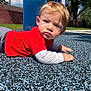 toddler, child, playground, outdoor, red_shirt, striped_pants, blue_trash_can, rubber_surface, sunny, grass, trees, face, hand, crawling, young_child, casual_clothing, daylight, expression, person, park