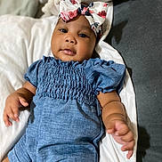 Kadora is registered to the contest to win money with this photo: baby, child, infant, blue_romper, headband, floral, bow, lying_down, cushion, white_bedding, portrait, indoors, cute, small_hands, soft_lighting, skin, face, eyes, expression, comfortable