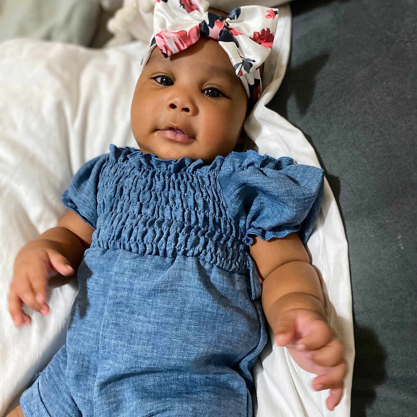 Kadora is registered to the contest to win money with this photo: baby, blue_romper, bow, child, comfortable, cushion, cute, expression, eyes, face, floral, headband, indoors, infant, lying_down, portrait, skin, small_hands, soft_lighting, white_bedding