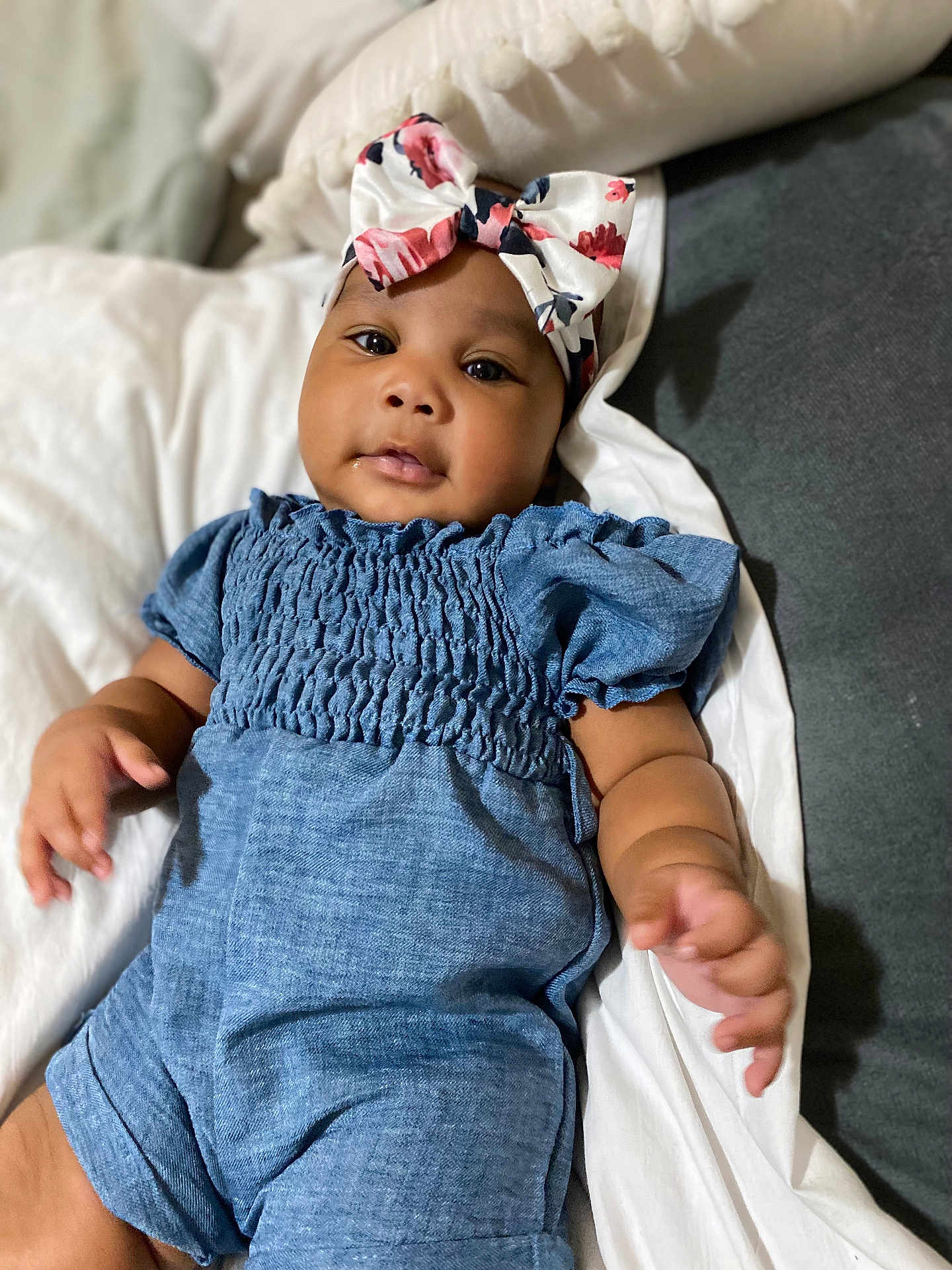 Kadora is registered to the contest to win money with this photo: baby, child, infant, blue_romper, headband, floral, bow, lying_down, cushion, white_bedding, portrait, indoors, cute, small_hands, soft_lighting, skin, face, eyes, expression, comfortable