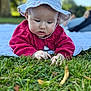 Eya a rejoint le concours — aidez-le/la à gagner de superbes lots ! baby, child, hat, red_sweater, blanket, grass, outdoor, nature, sunhat, exploring, curious, person, face, hands, greenery, daylight, young_child, candid, portrait, closeup