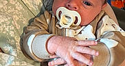 Mason joined the competition — help win amazing prizes! baby, pacifier, onesie, bear_pattern, hands, person, clothing, floral_shirt, indoor, face, infant, cute, child, newborn, portrait, holding, skin, expression, closeup, hand_gesture