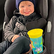 Wyatt is registered to the contest to win money with this photo: child, toddler, car_seat, hat, smile, toy_story, sippy_cup, jacket, seatbelt, car_interior, happy, blue_eyes, clothing, young_child, portrait, casual, kid, seat, cozy, travel