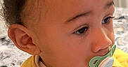 Elias joined the competition — help win amazing prizes! toddler, child, baby, portrait, pacifier, yellow_clothing, sweater, indoor, sitting, face, hair, curly_hair, brown_hair, eyes, nose, ear, baby_clothing, buttons, bedroom, cozy