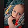 baby, infant, child, car_seat, quilted, gray, red_clothing, fingers, blue_eyes, face, portrait, sitting, indoors, cute, young_child, closeup, comfort, seatbelt, head_support, expression