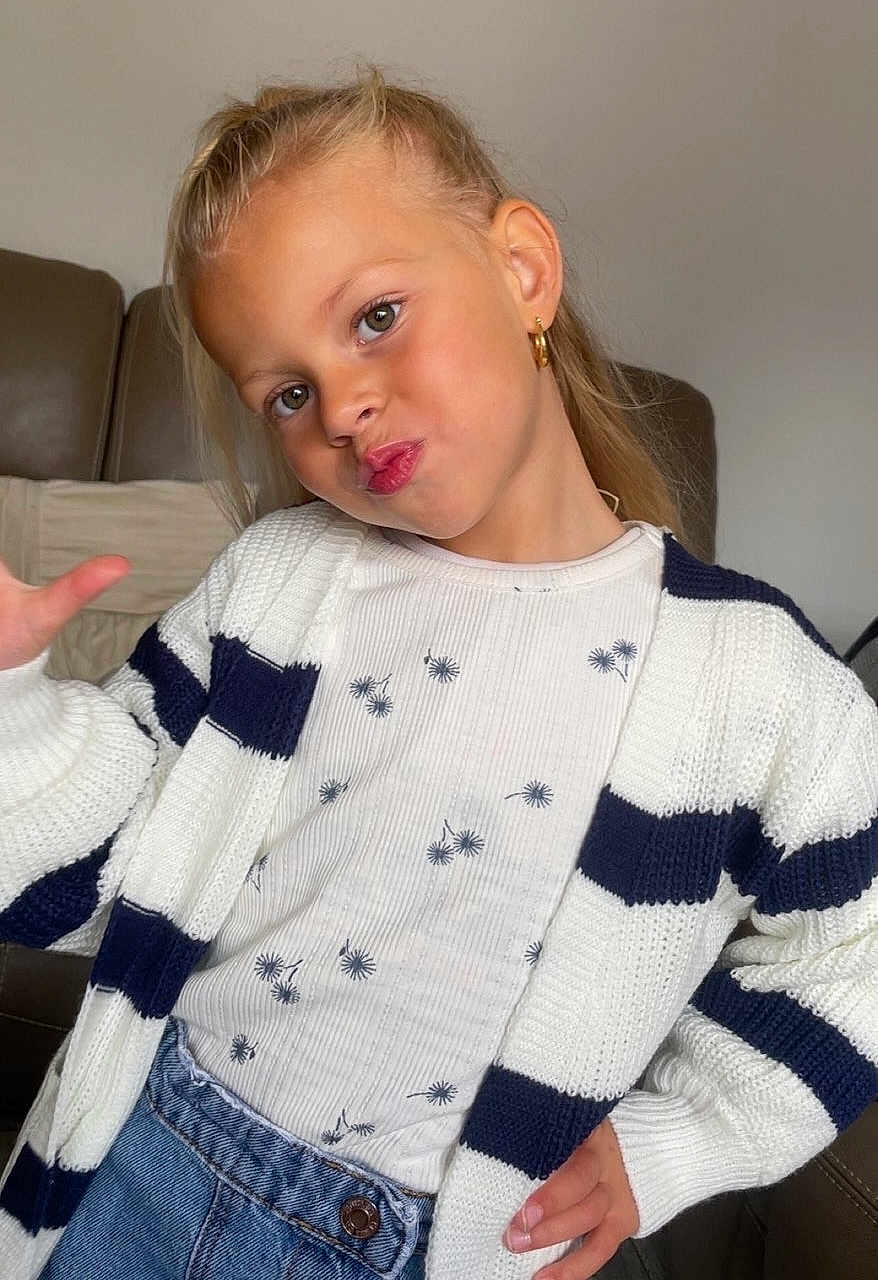 Mya participe au concours pour gagner de l'argent avec cette photo : child, girl, playful, pose, cardigan, striped_clothing, long_hair, earrings, indoor, couch, casual_clothing, denim, hand_gesture, smiling, portrait, fashion, young, light_skin, happy, home