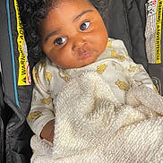 Journey is registered to the contest to win money with this photo: baby, child, curly_hair, blanket, car_seat, warning_label, clothing, cute, infant, portrait, indoors, young_child, cozy, expression, looking_up, seat, soft_texture, toddler, person, close_up
