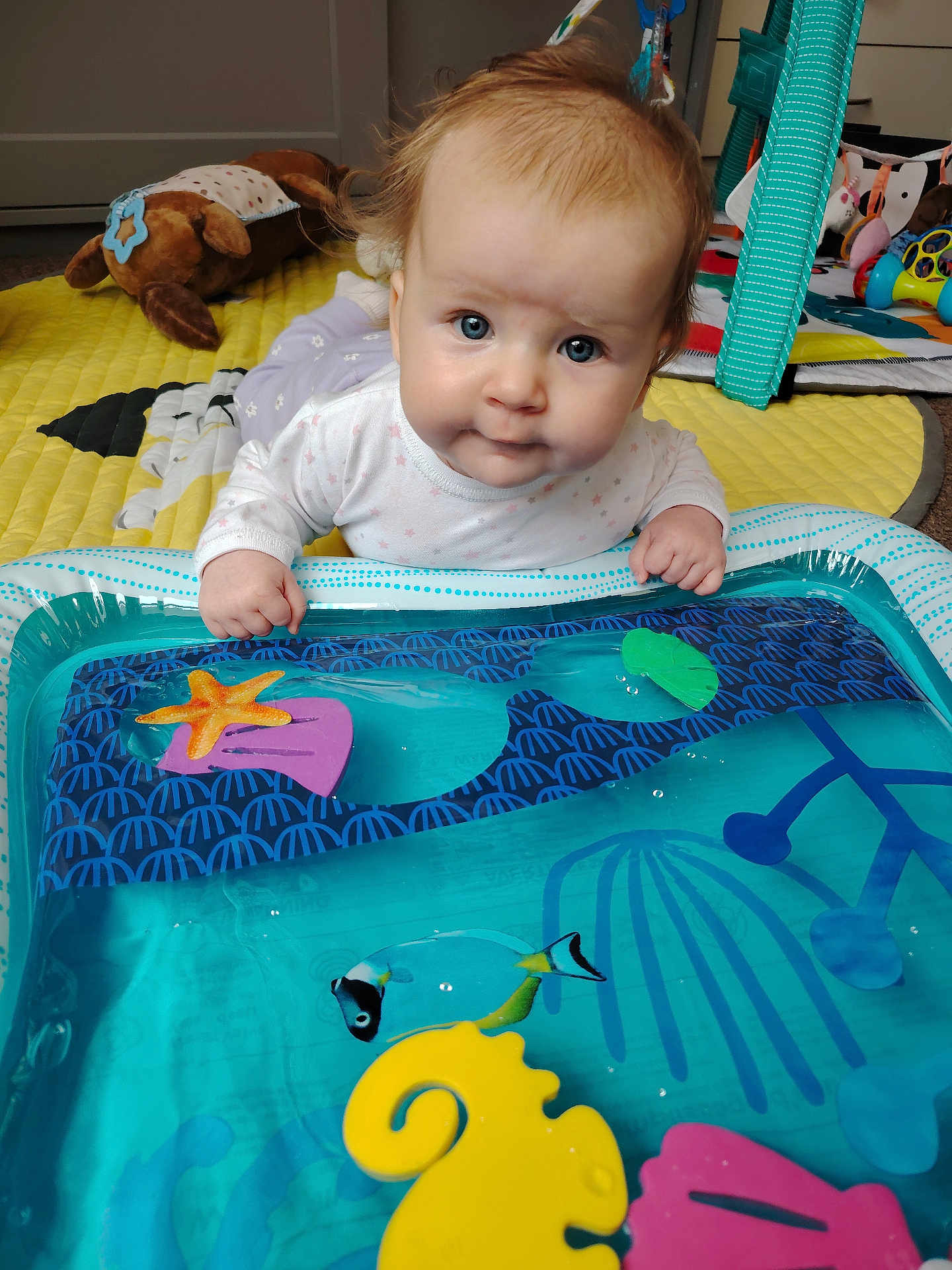 Lidia joined the competition — help win amazing prizes! baby, blue_eyes, water_mat, toy, indoor, play_area, colorful, infant, curious, soft_lighting, carpet, plush_toy, hand, face, clothing, floor, child, early_childhood, playtime, crawling