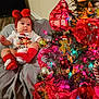baby, infant, christmas_tree, holiday_decorations, red_bow, red_socks, bean_bag, wooden_floor, ornaments, ribbons, lights, festive, indoor, cute, child, smiling, christmas, holiday, decoration, celebration