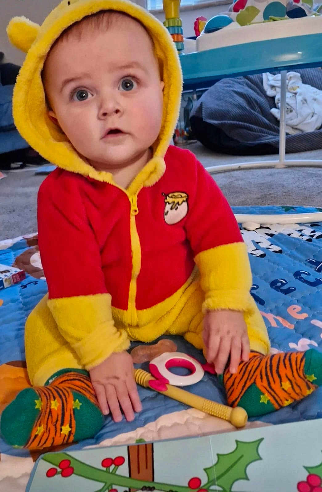 Albert is registered to the contest to win money with this photo: baby, child, hooded_clothing, red, yellow, sitting, play_mat, toy, indoor, curious, face, person, sock, striped_sock, floor, carpet, hand, infant, cute, expression