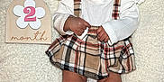 Sariyah is registered to the contest to win money with this photo: baby, infant, plaid_skirt, white_top, red_bow, headband, red_socks, bows, wooden_sign, number_two, month, blanket, soft_texture, cute, lying_down, wide_eyes, curious, child, portrait, adorable