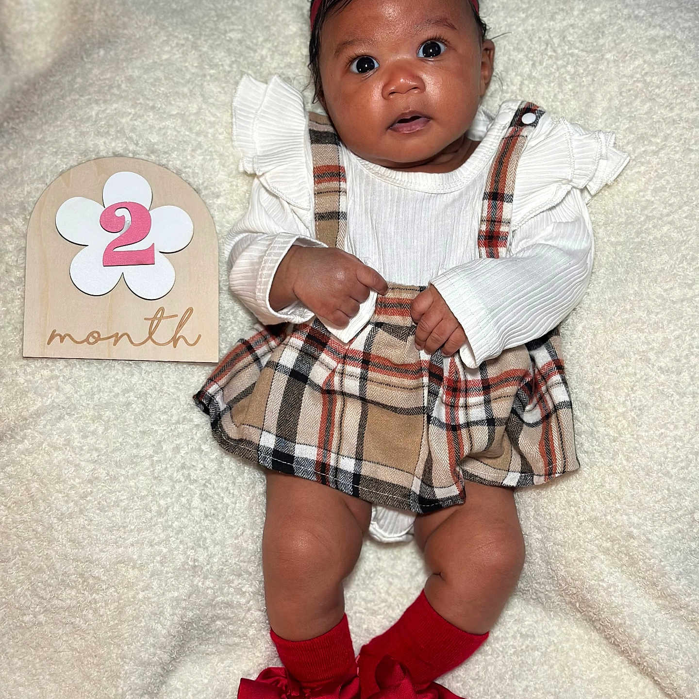 Sariyah is registered to the contest to win money with this photo: adorable, baby, blanket, bows, child, curious, cute, headband, infant, lying_down, month, number_two, plaid_skirt, portrait, red_bow, red_socks, soft_texture, white_top, wide_eyes, wooden_sign