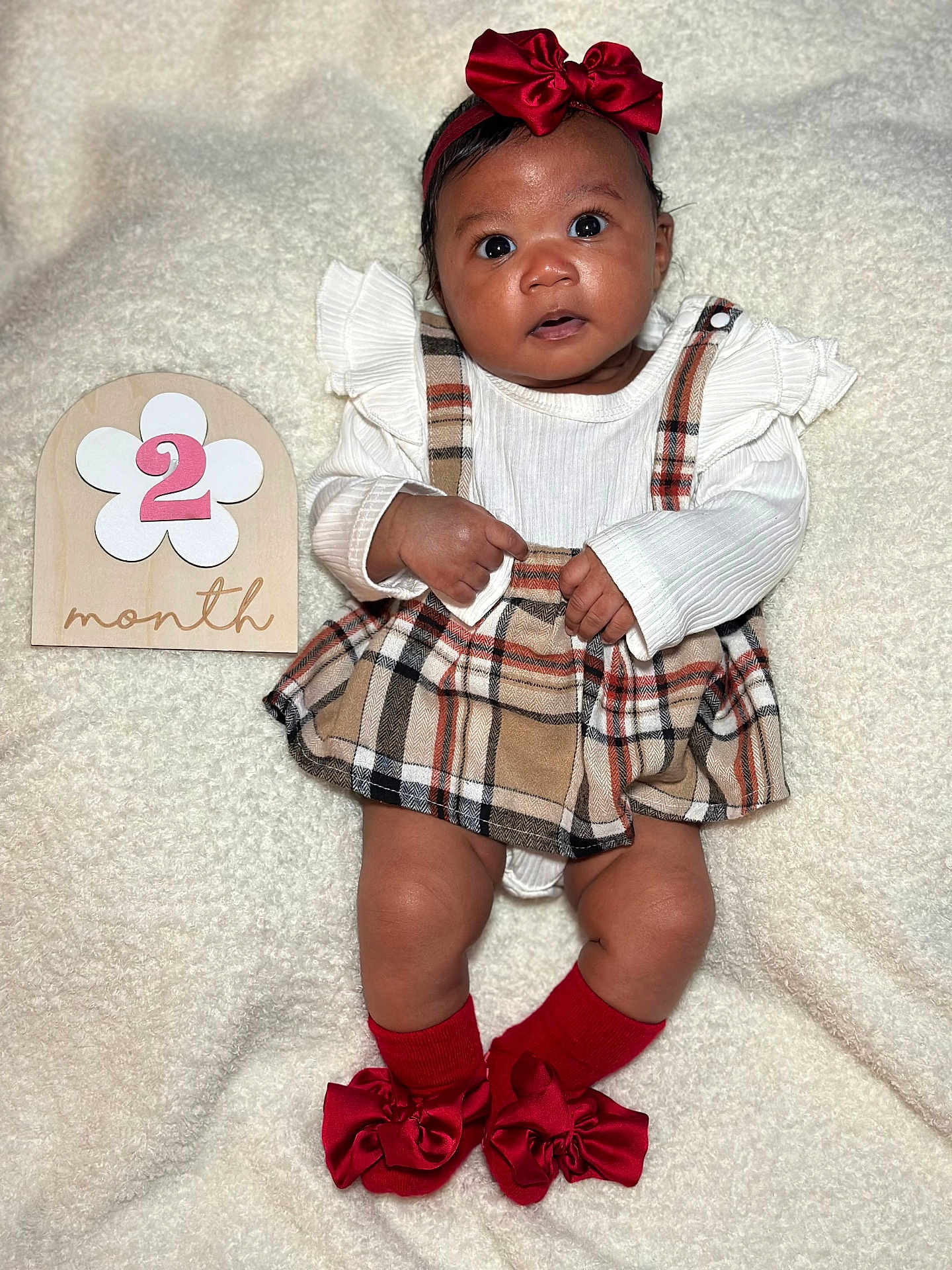 Sariyah is registered to the contest to win money with this photo: baby, infant, plaid_skirt, white_top, red_bow, headband, red_socks, bows, wooden_sign, number_two, month, blanket, soft_texture, cute, lying_down, wide_eyes, curious, child, portrait, adorable