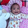 Sariyah joined the competition — help win amazing prizes! baby, smiling, infant, onesie, bonnet, blanket, plush_toy, pacifier, cute, happy, lying_down, patterned_clothing, pink, soft_toy, child, indoors, portrait, face, sleepwear, cozy