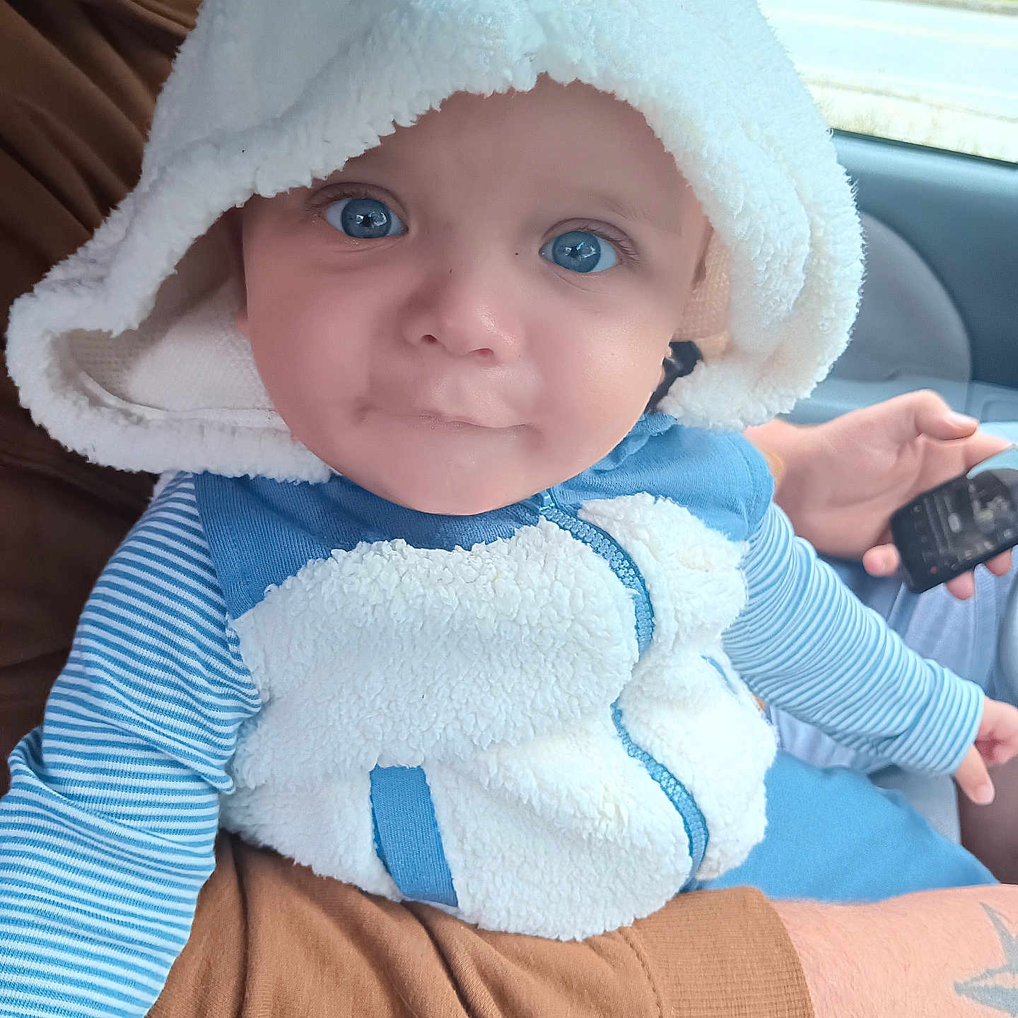 Logan is registered to the contest to win money with this photo: baby, bodypart, bonnet, clothing, electronics, face, finger, hand, hat, head, hood, hoodie, knitwear, mobilephone, person, phone, photography, portrait, sweater, sweatshirt