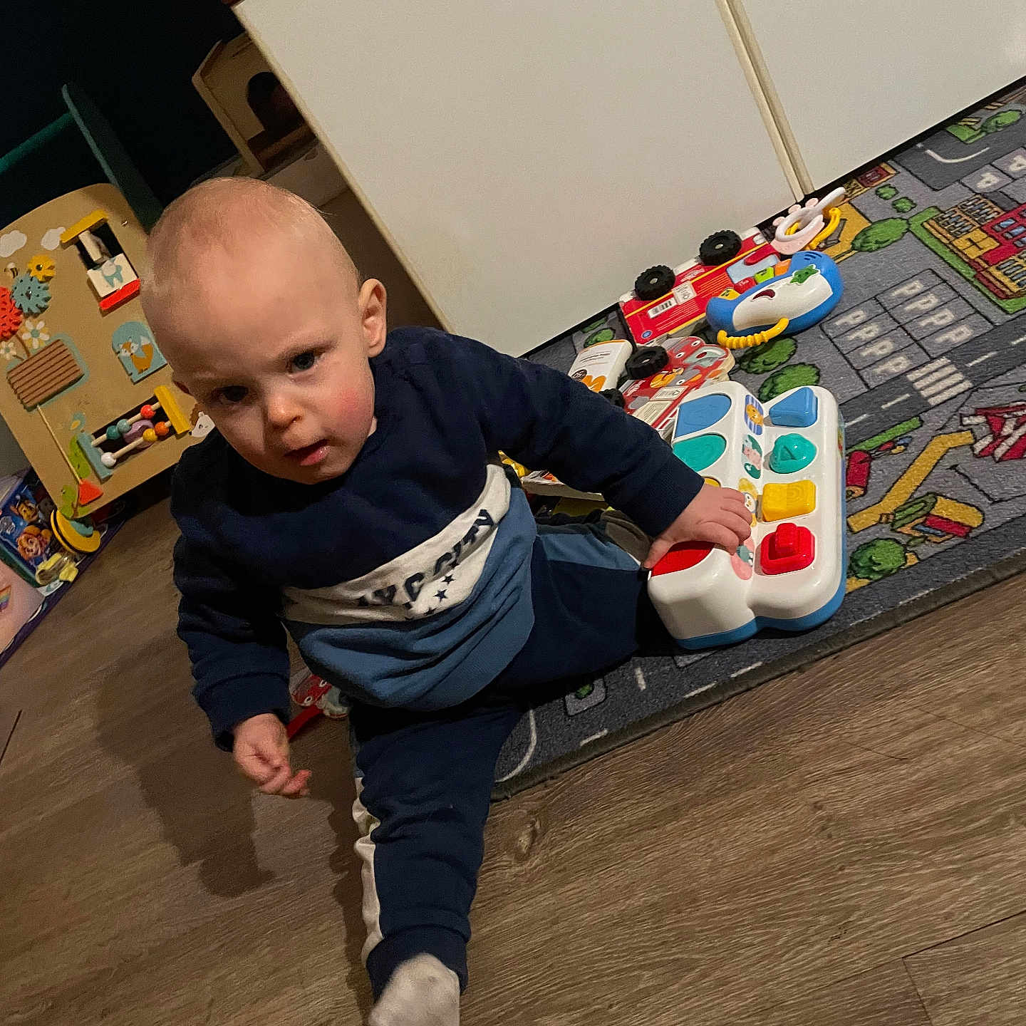 Eljy a rejoint le concours — aidez-le/la à gagner de superbes lots ! cabinet, child, clothing, colorful, curious, expression, floor, furniture, indoor, person, piano_toy, play, playmat, room, sitting, sock, toddler, toy, wooden_floor, young_child