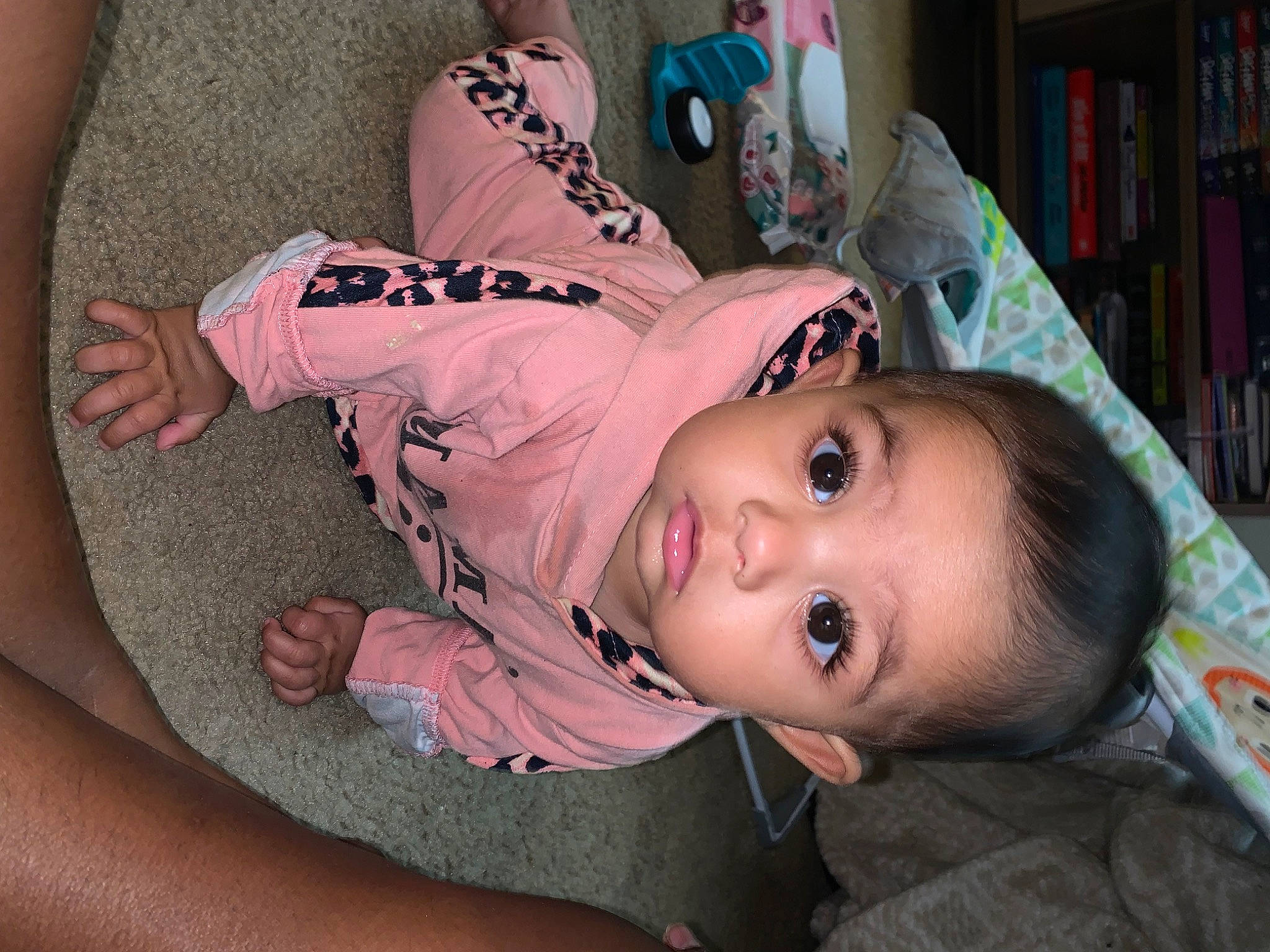 Amari is registered to the contest to win money with this photo: baby, bookcase, cheek, child, eyelash, flooring, fun, fur, happy, human_leg, knee, pattern, person, pink, shelf, shelving, sitting, skin, thigh, toddler