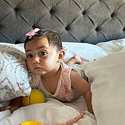 Ayla is registered to the contest to win money with this photo: baby, child, toy, bed, blanket, pillow, headboard, pink_bow, curious, indoors, soft_light, infant, clothing, plaything, sleeping_area, toddler, cute, portrait, person, resting